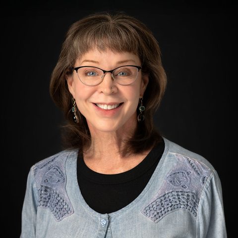 Rhonda Alton-Tracy, smiling, wearing glasses and a pale blue linen jacket.